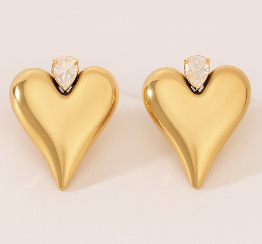 Gold heart-shaped earrings with clear gemstones on a light background