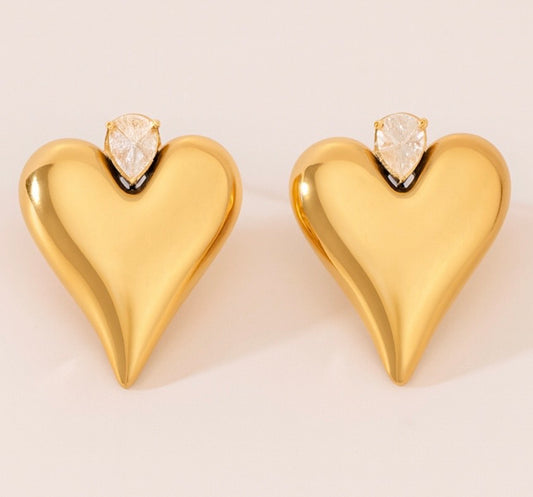 Gold heart-shaped earrings with clear gemstones on a light background